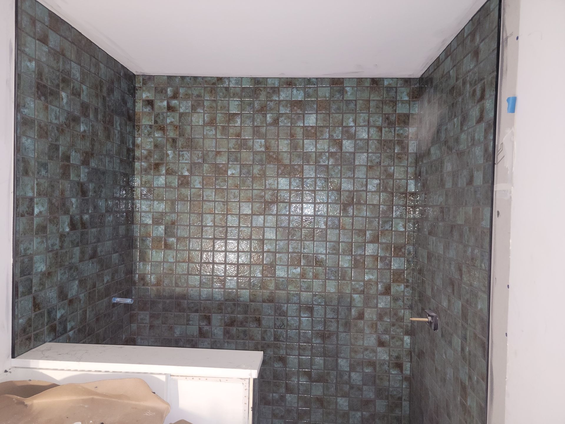 Shower walls tiled with mottled blue-green squares, with a silver fixture visible.