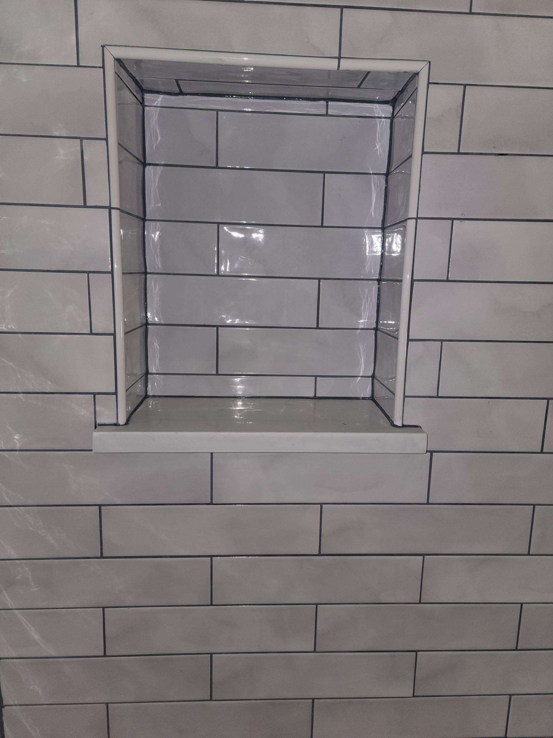 Recessed shower niche with white rectangular tiles and dark grout.