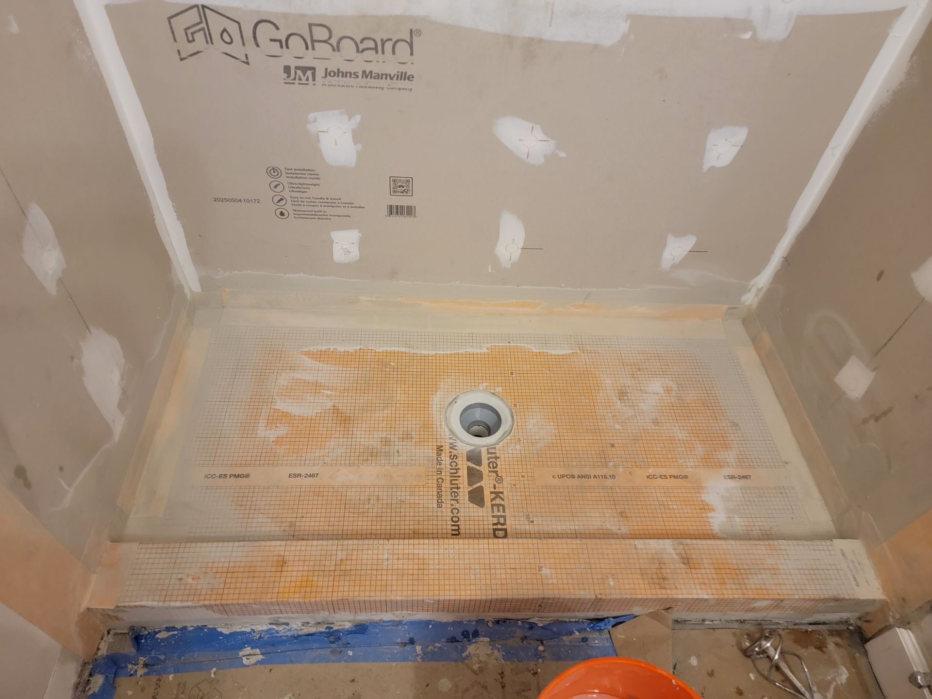 Shower stall with a pre-sloped floor and drain, ready for tile installation, set against drywall walls.