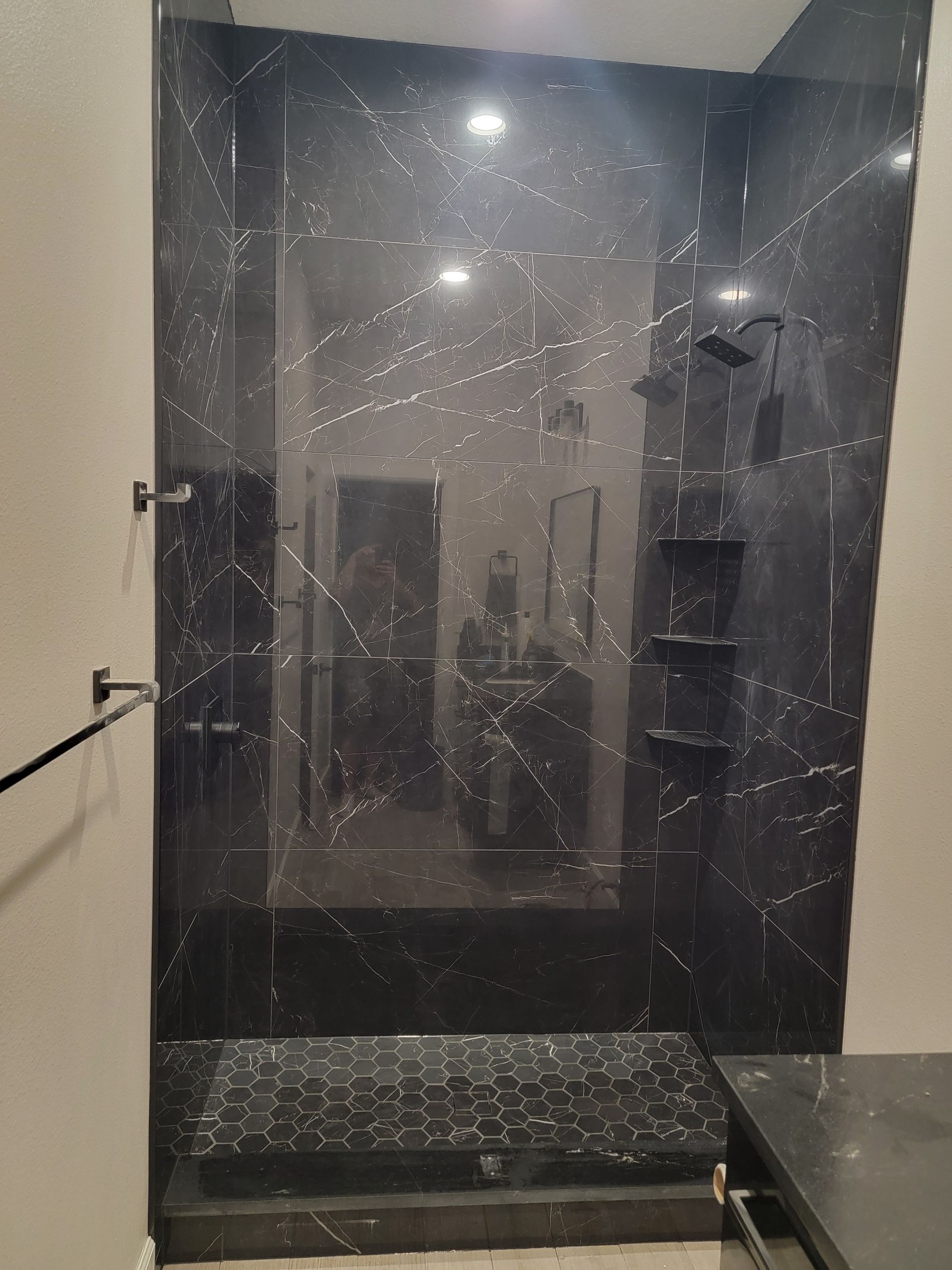 Black marble shower with glass door and shelving.