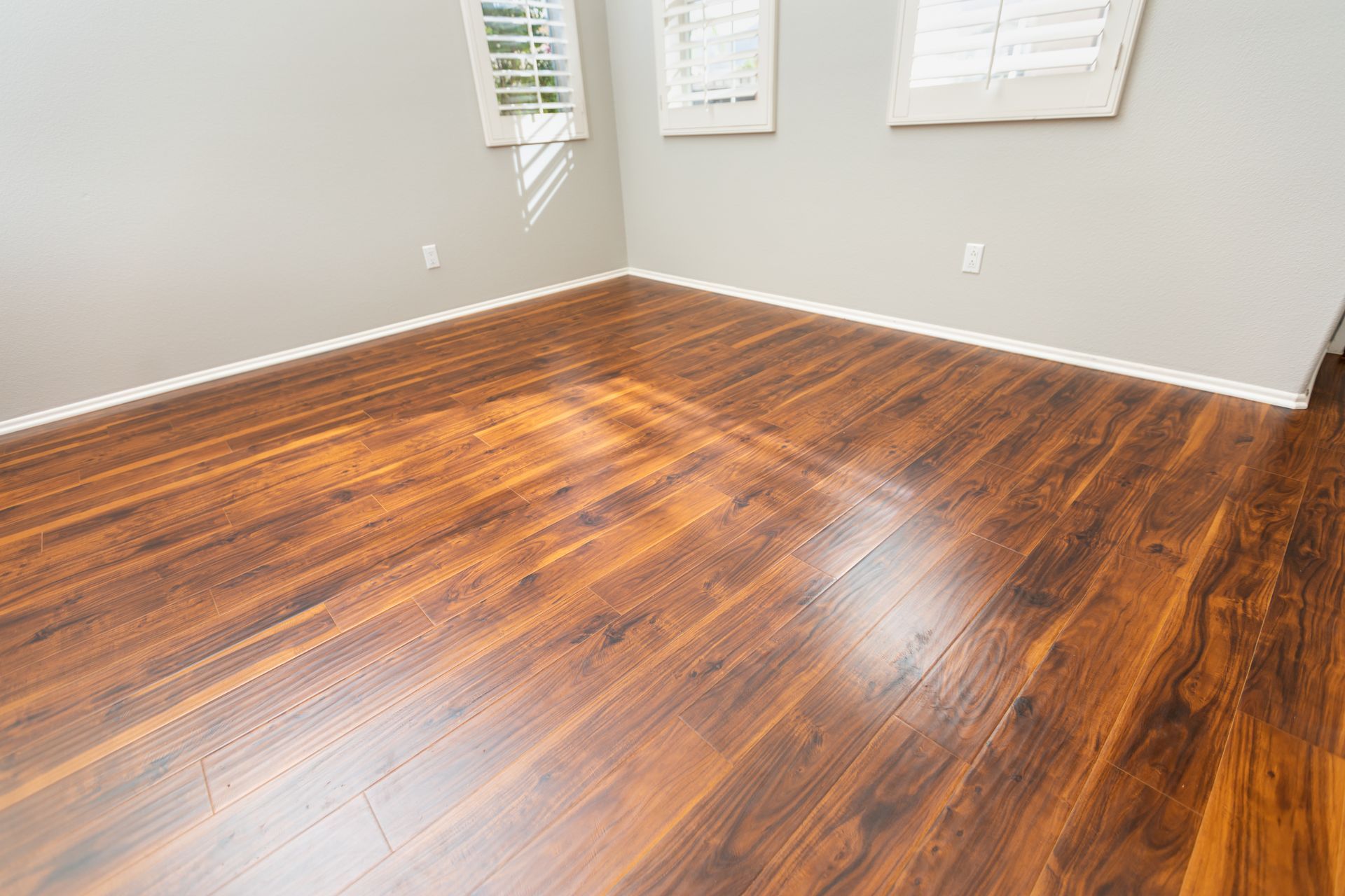 Empty room with brown wooden floor, grey walls, and white-shuttered windows.
