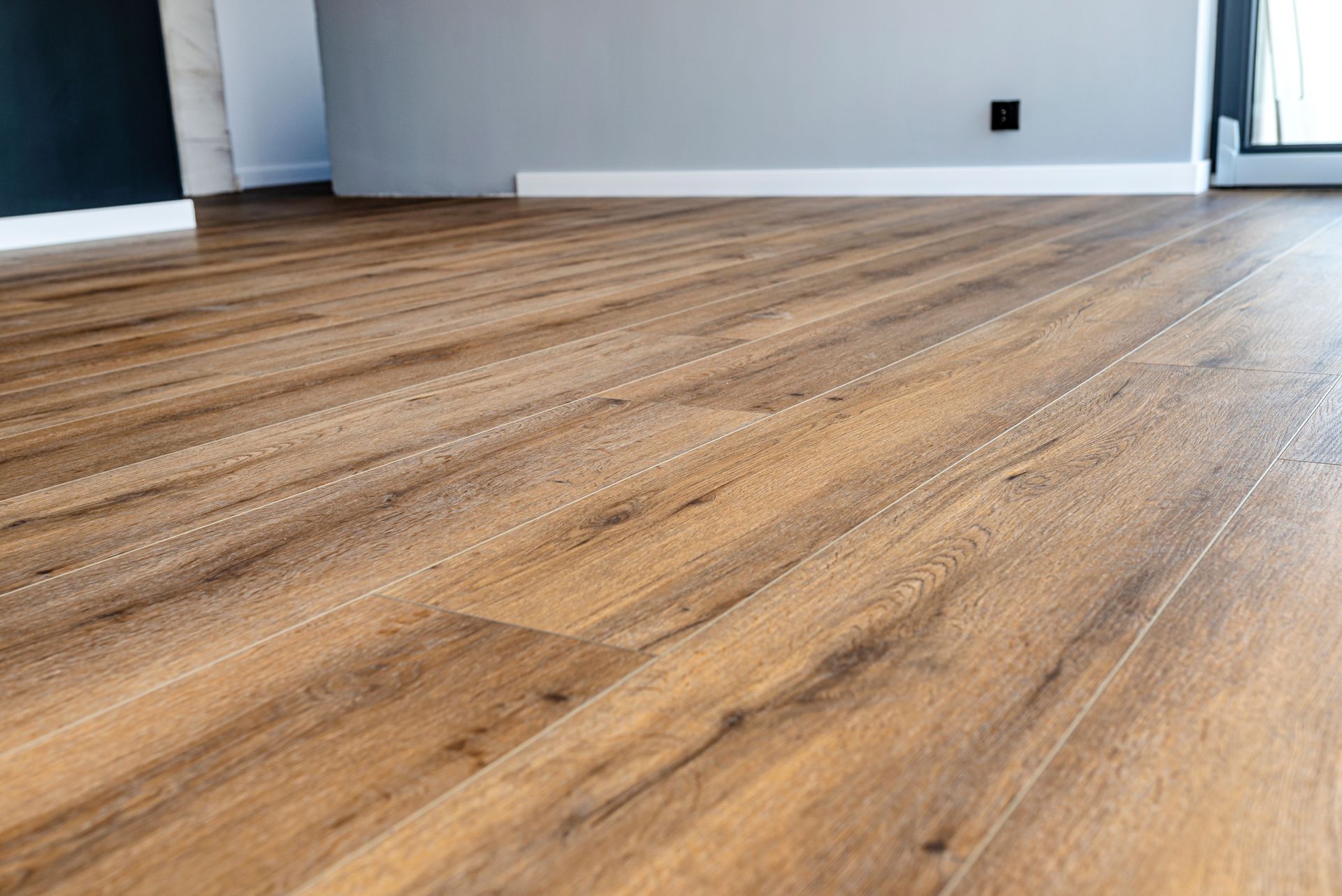 Close-up of a brown, wood-look laminate floor. Gray and white walls are in the background.