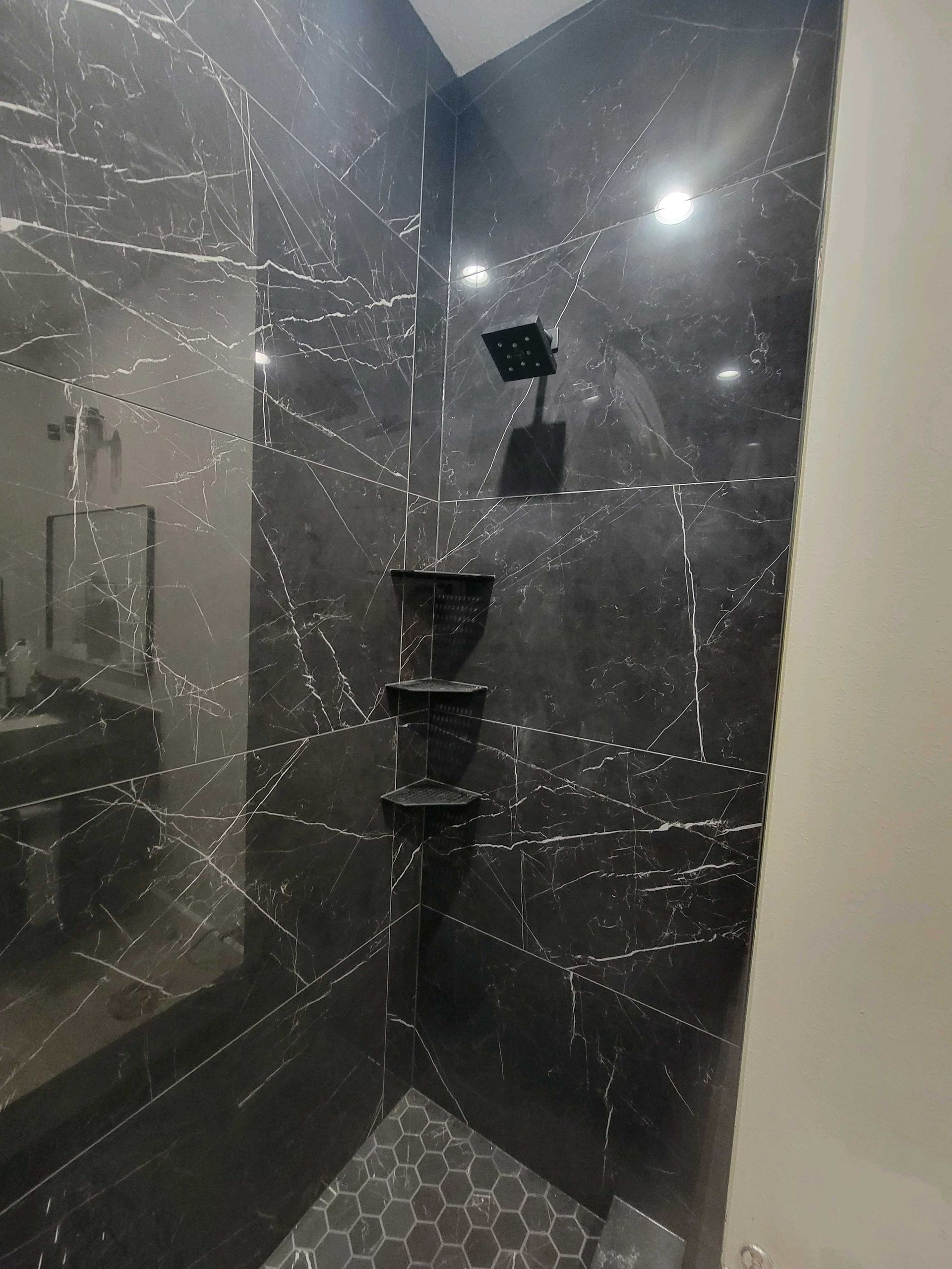 Black marble shower with hexagonal floor tiles and corner shelves.