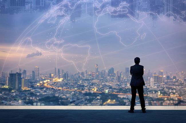 A man is standing on top of a building overlooking a city at night.