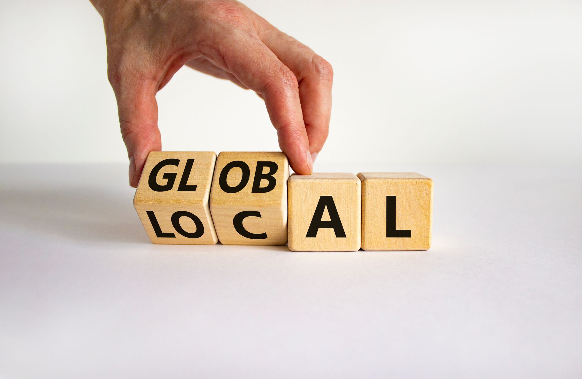 A hand is holding wooden blocks with the words global local written on them.