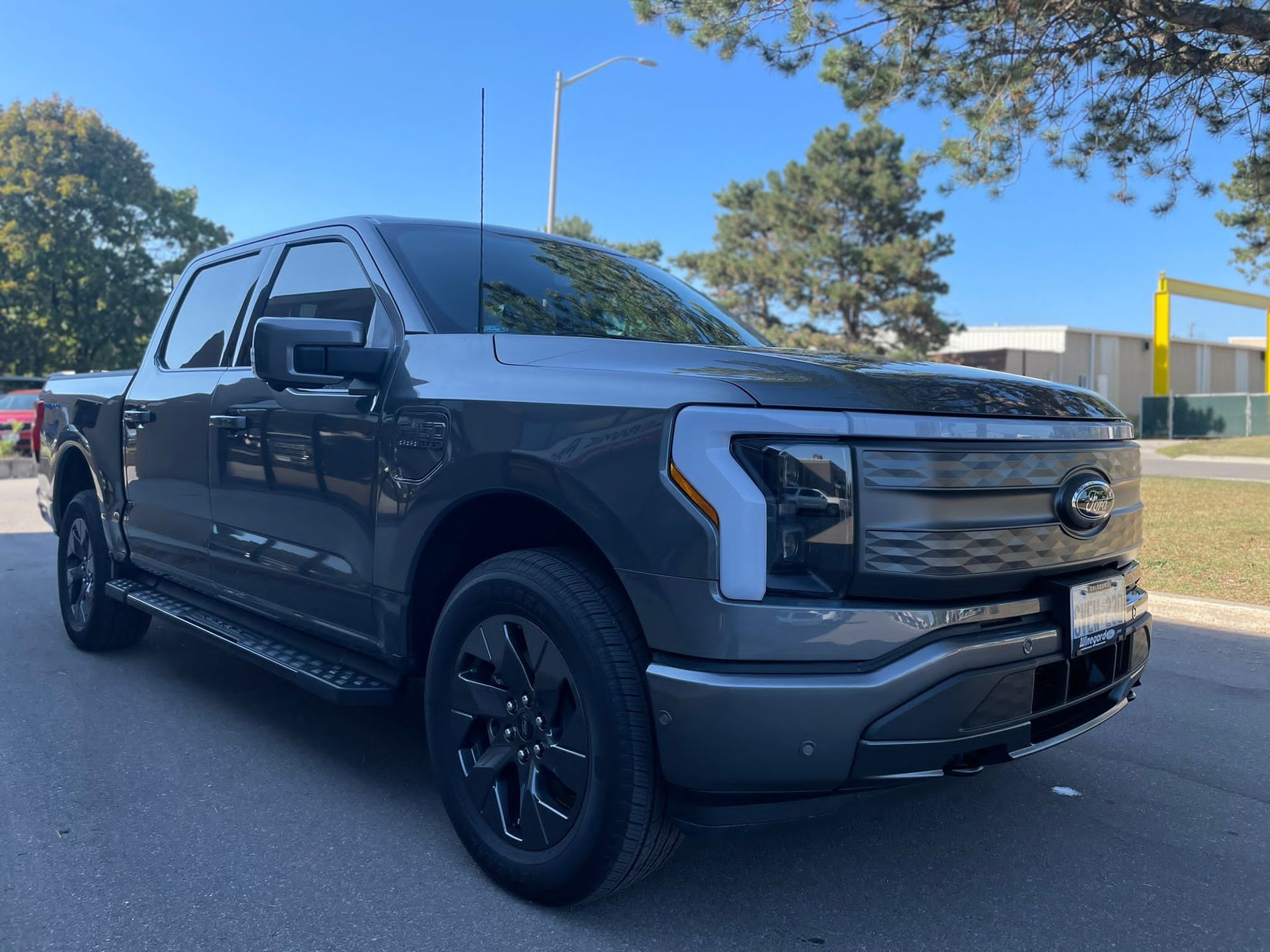 A grey Ford F-150 Lightning electric pickup truck parked on an asphalt road under a clear blue sky.