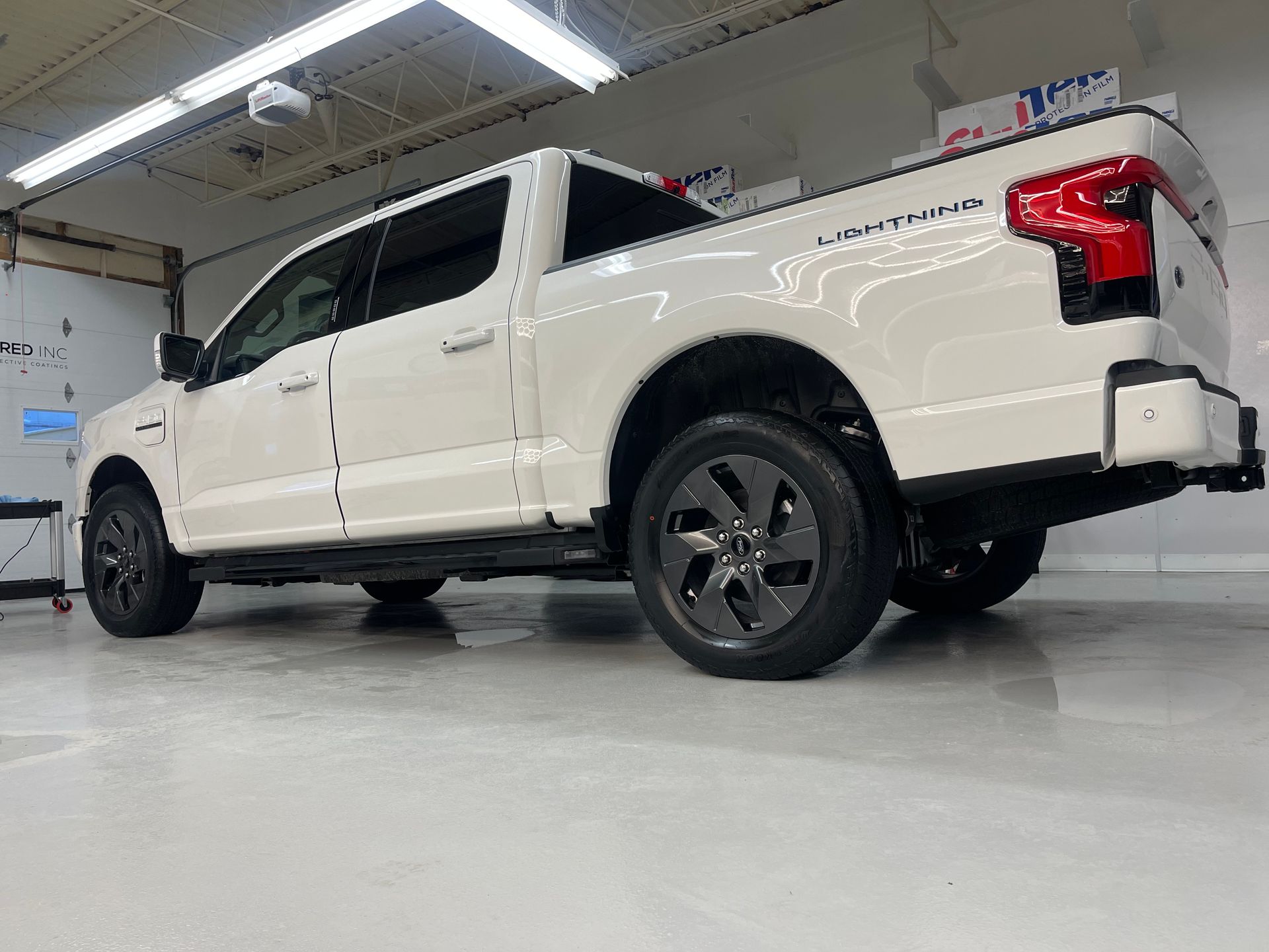 A white Ford F-150 Lightning electric pickup truck parked indoors in a bright garage setting.