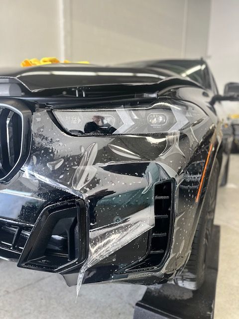 The front of a black car is covered in plastic.