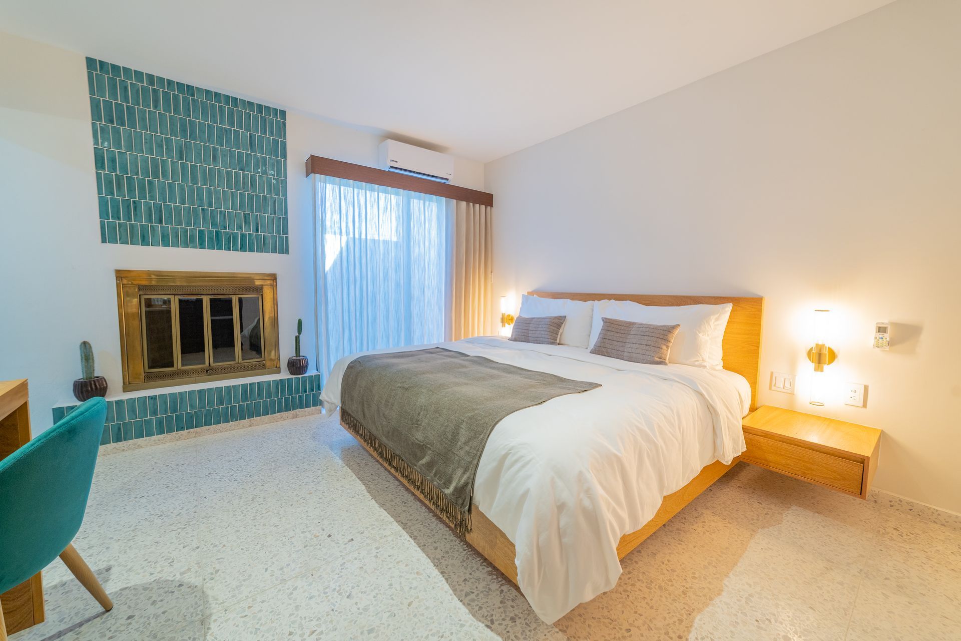 Dormitorio con una cama, chimenea con azulejos de color verde azulado y un escritorio con una silla de color verde azulado.