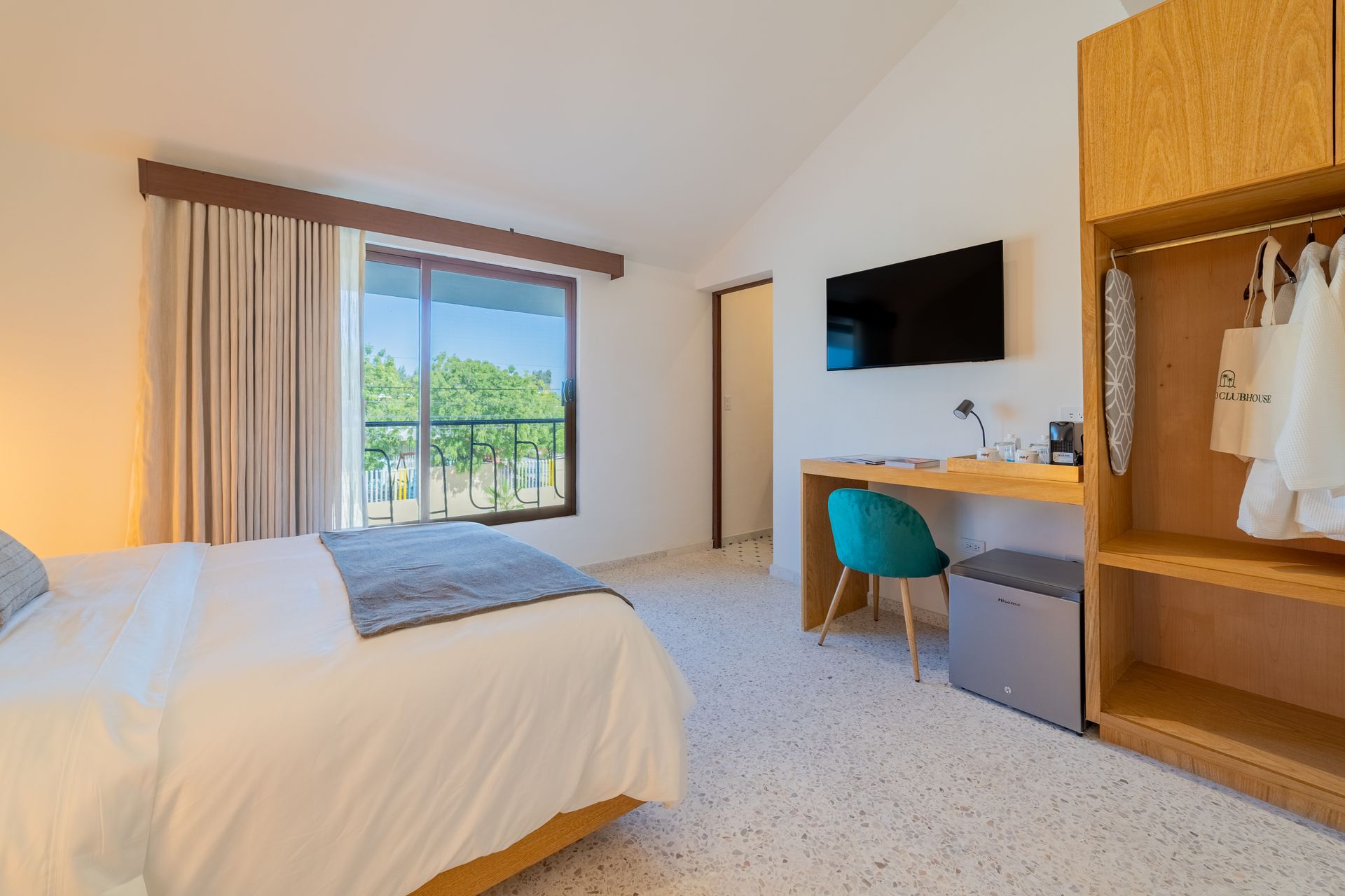 Interior de dormitorio con cama, escritorio, armario, ventana y TV.