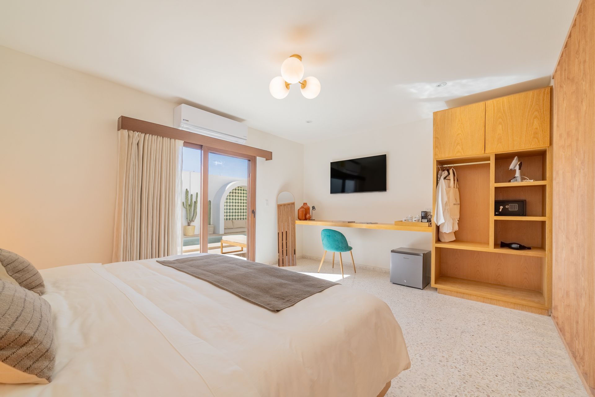 Dormitorio con cama, escritorio, armario y balcón con vistas al patio. Paredes blancas y armario beige.