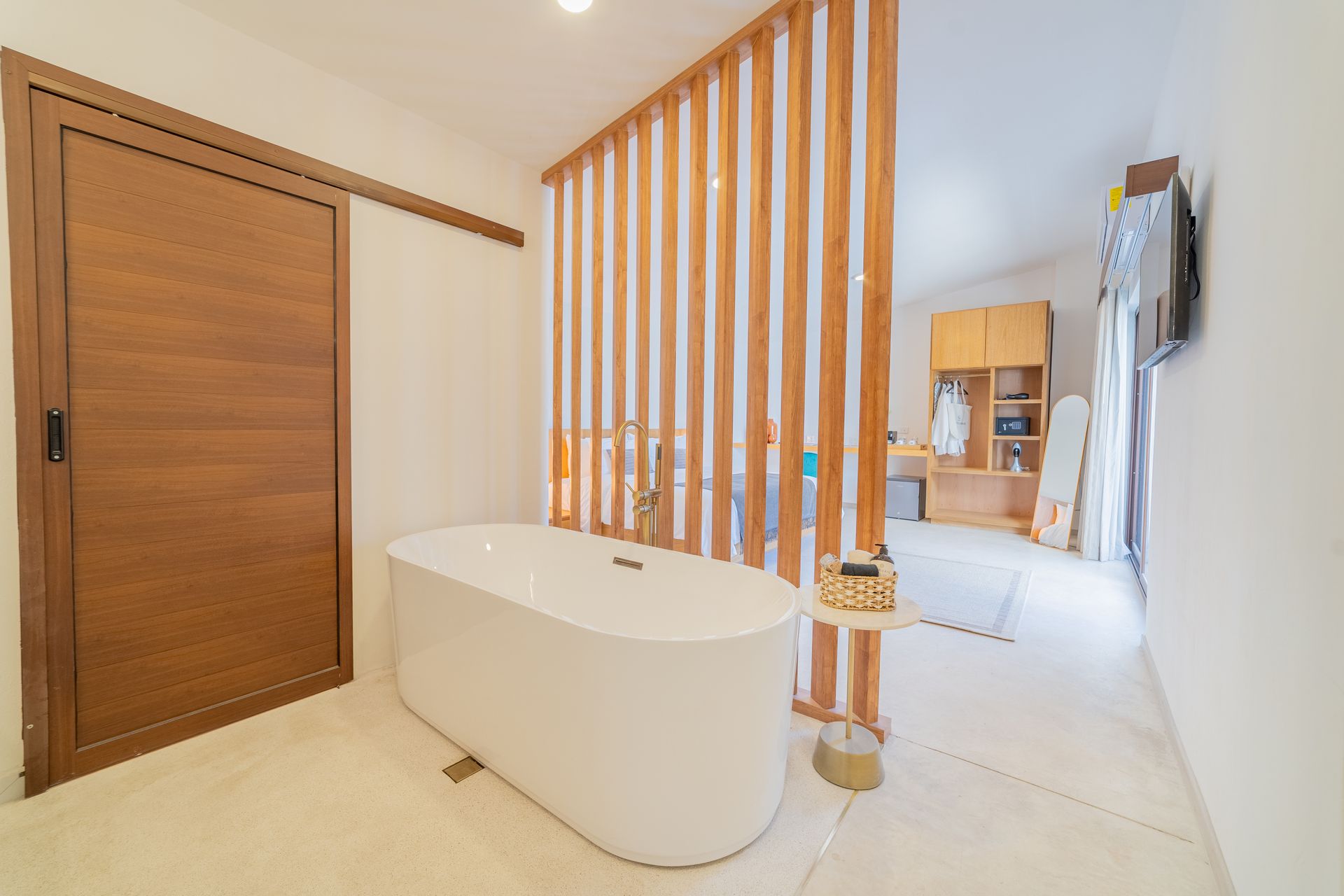 Baño con bañera blanca, puerta de madera y mampara de lamas de madera que lo separa de un dormitorio.