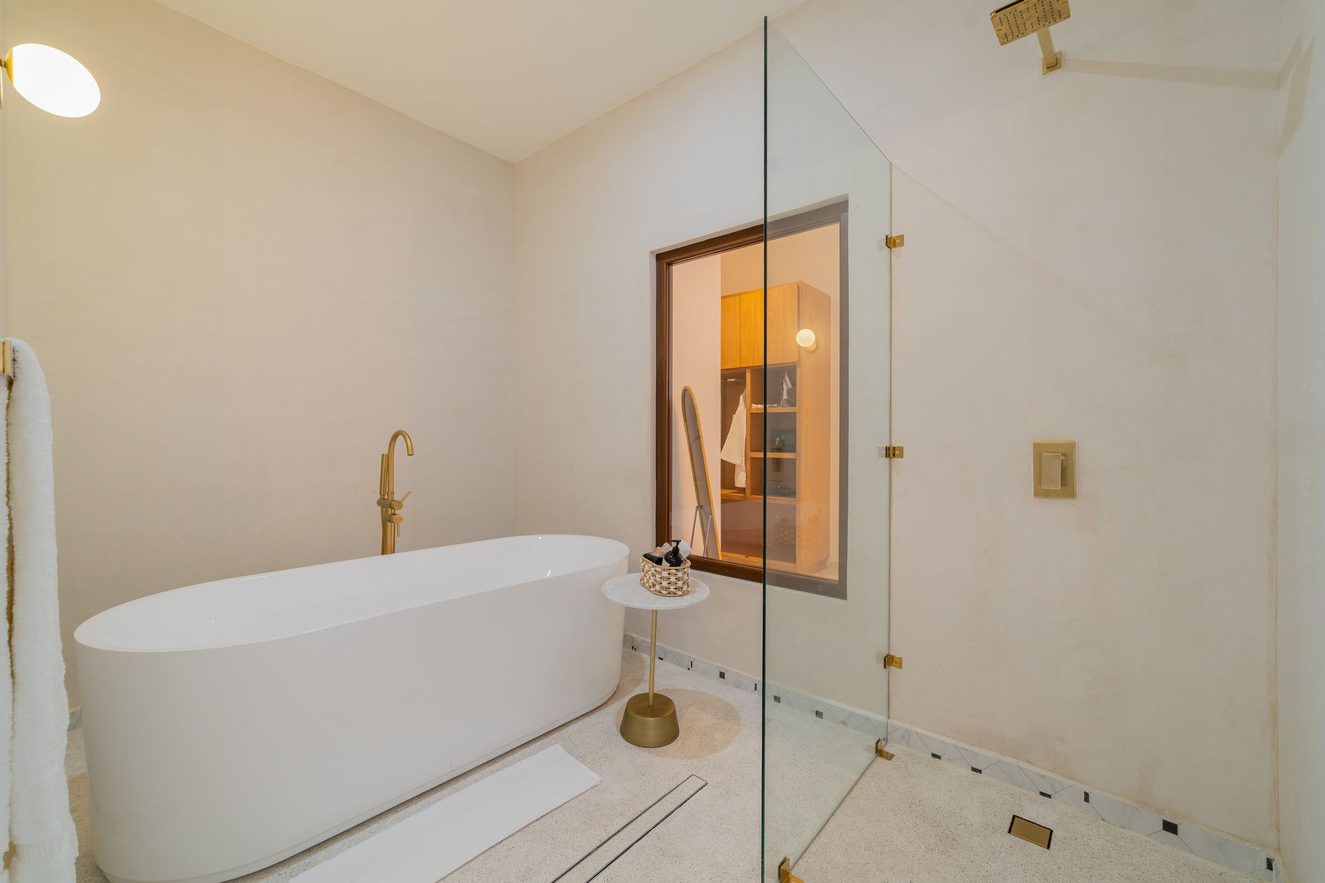 Baño moderno con bañera independiente blanca, accesorios dorados y ducha de cristal.