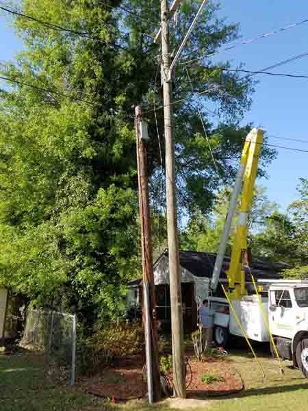 A crane is working on a power pole in front of a house.