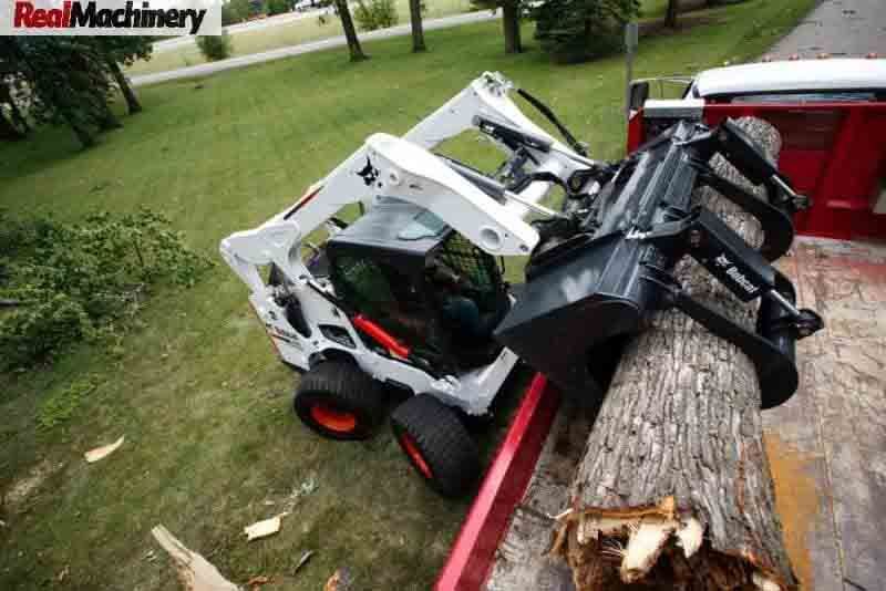 A bobcat is carrying a log on a trailer.