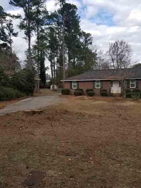 A brick house with a lot of grass in front of it and trees in the background.