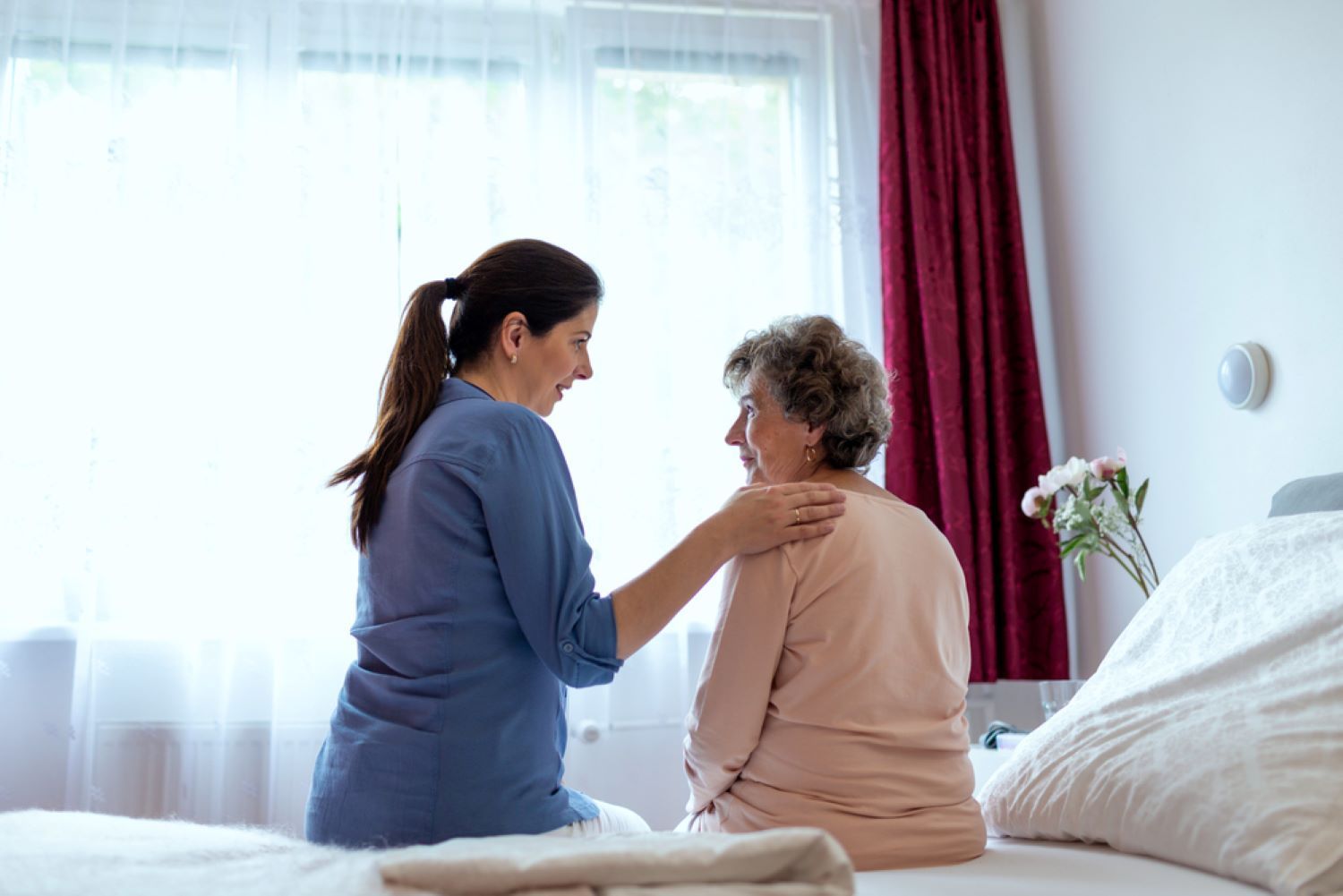 A Nurse is Talking to an Elderly Woman Sitting on a Bed — Supportability Care Services in West Rockhampton, QLD