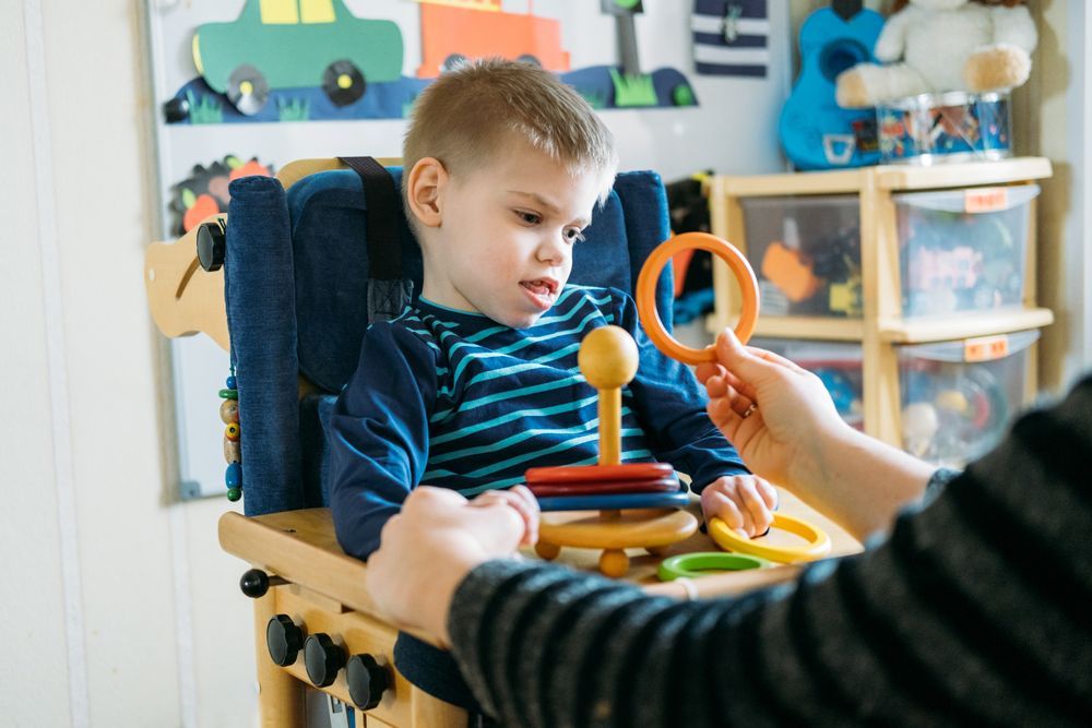 A Young Boy is Sitting in a High Chair Playing — Supportability Care Services in West Rockhampton, QLD
