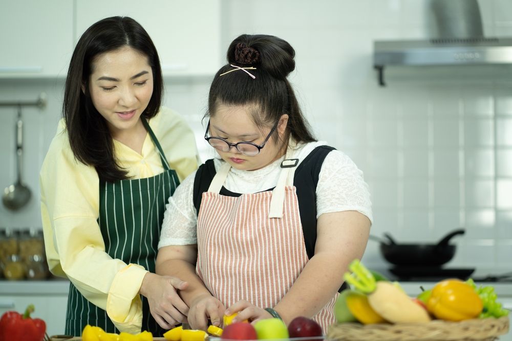 A Woman is Helping a Girl With Down Syndrome Prepare Food — Supportability Care Services in West Rockhampton, QLD
