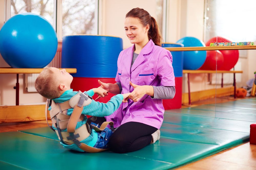A Woman is Sitting on the Floor With a Child in a Harness — Supportability Care Services in West Rockhampton, QLD