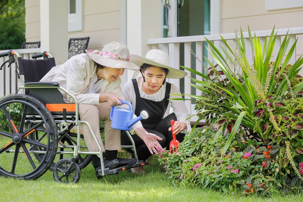 A Woman in a Wheelchair is Watering Flowers With a Little Girl — Supportability Care Services in West Rockhampton, QLD