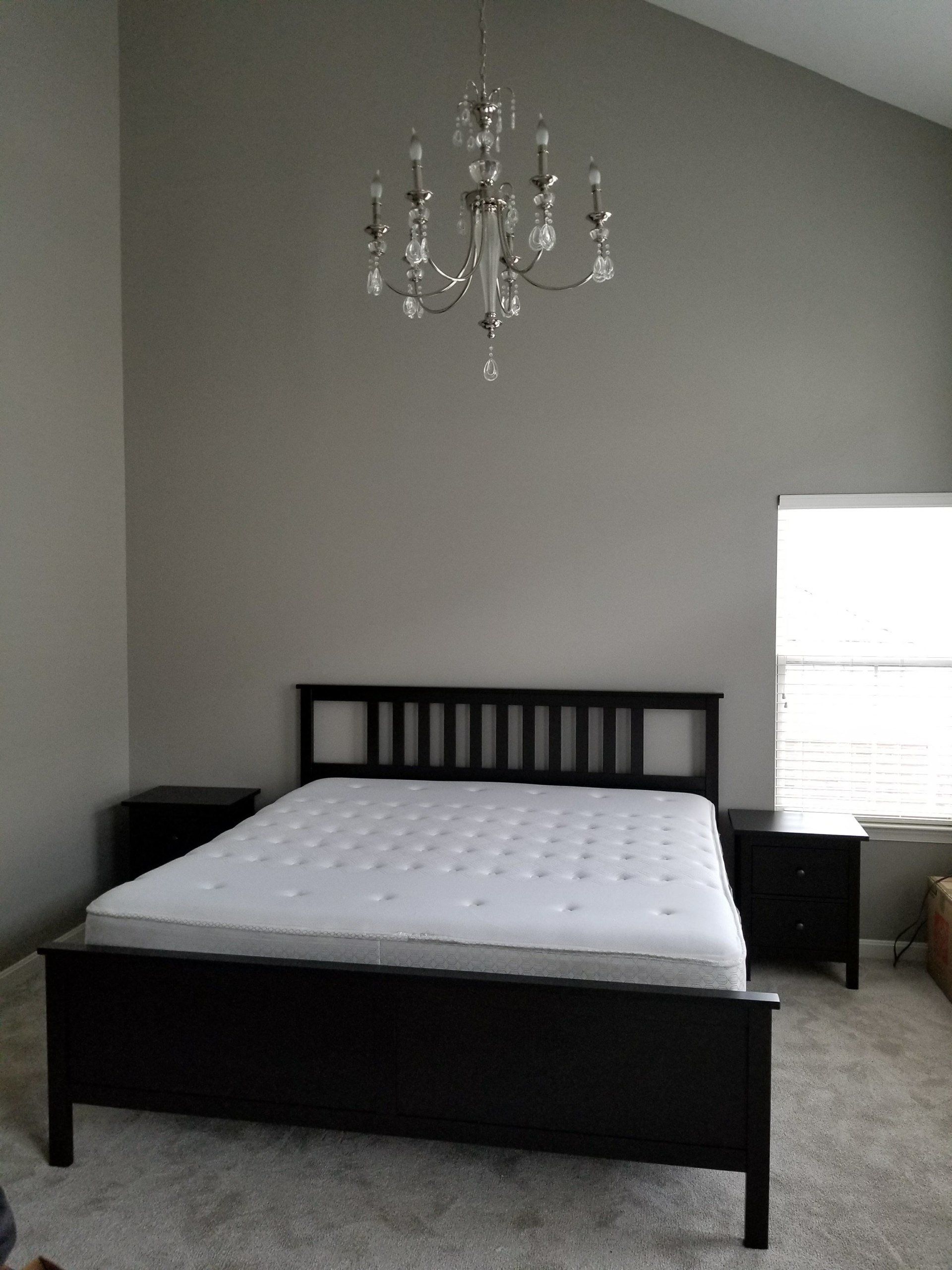 Bedroom with a black bed, nightstands, and a chandelier against a gray wall, a window on the right.