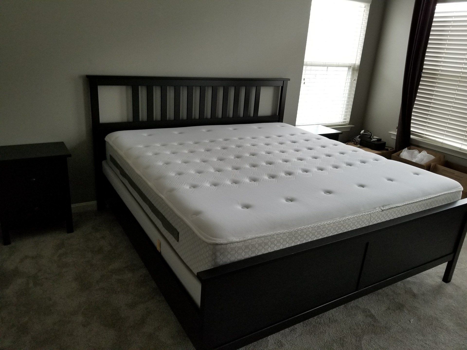 Black bed frame with mattress and nightstand in a bedroom with a window.