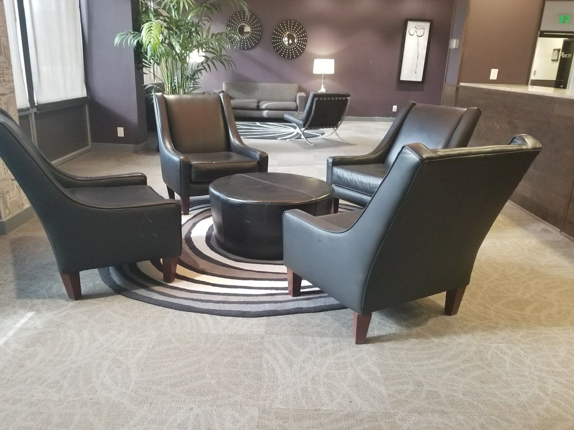 Four black leather chairs around a round table on a circular rug in a waiting room.