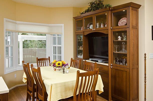 A dining room with a table covered in a yellow cloth, surrounded by wooden chairs, next to a large wooden display cabinet.
