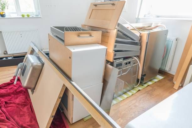 Kitchen renovation in progress with dismantled cabinets and a dishwasher piled on a red cloth and wood floor.