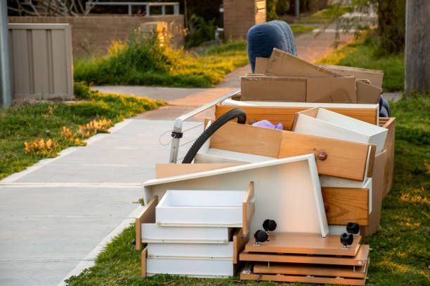 Heap of discarded dresser drawers and boxes piled on a sidewalk curb. Person bends over the pile.