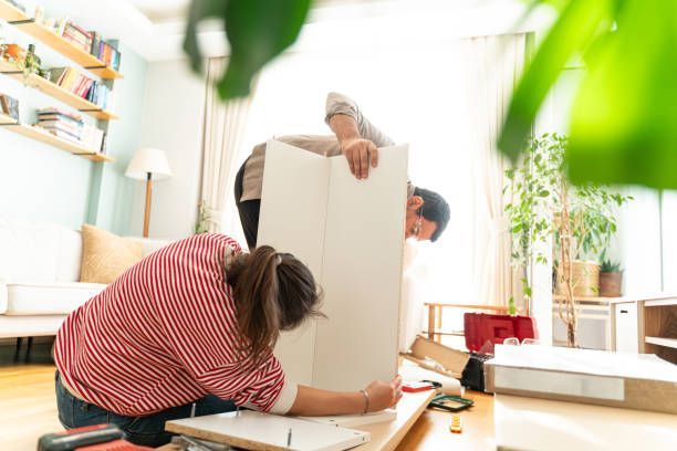 People assembling furniture in a bright living room, with tools and boxes on the floor.