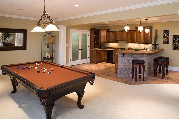 Pool table in a basement with a bar, stools, and cabinetry; neutral-toned walls and floor.