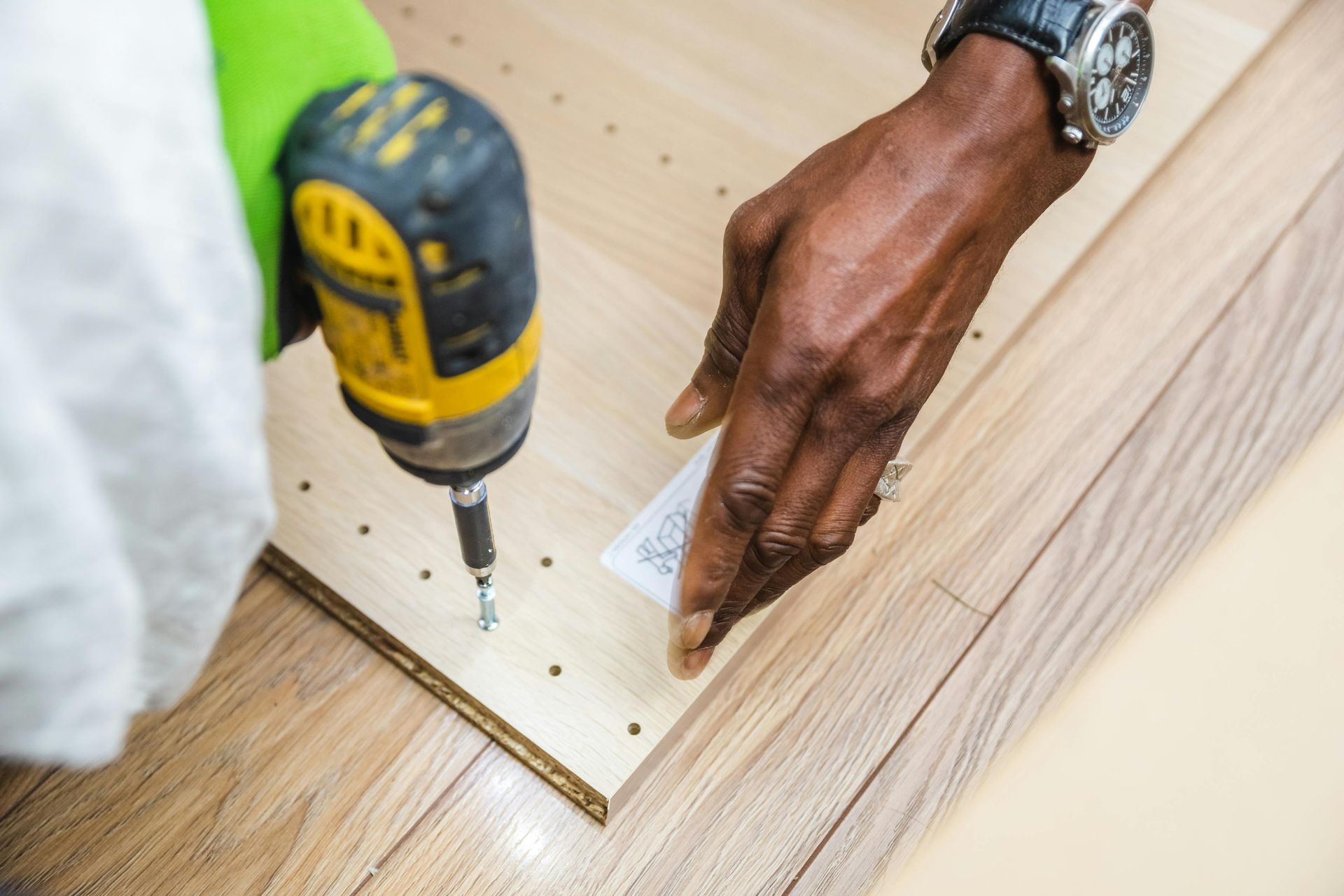 A close-up of a person using a yellow power drill to fasten a screw into a pre-drilled light wood panel.