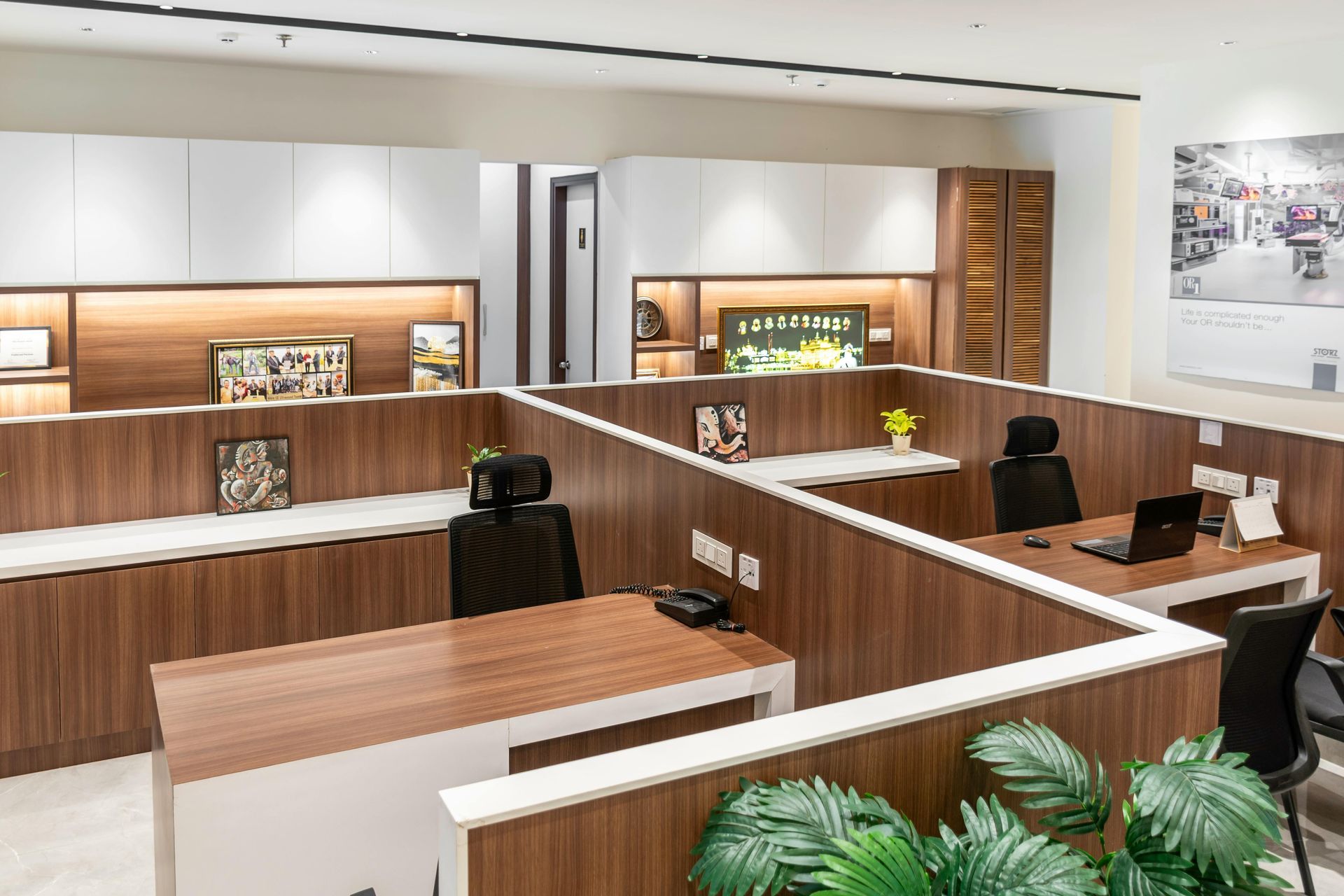 Modern office reception area with wood desks, black chairs, warm lighting, and potted plants