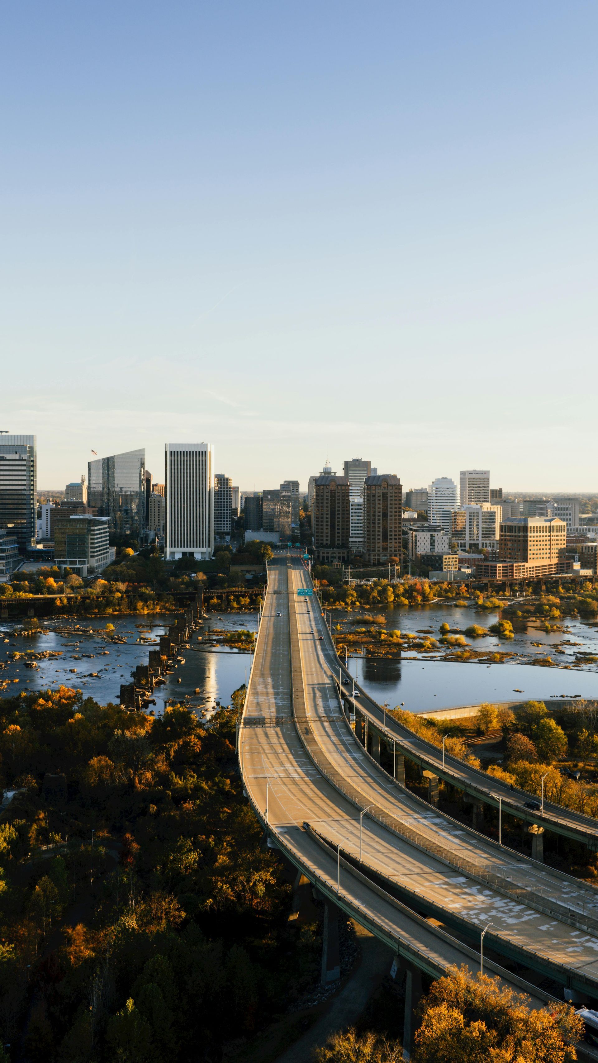 City skyline at dusk with a curving bridge over water and traffic in the foreground