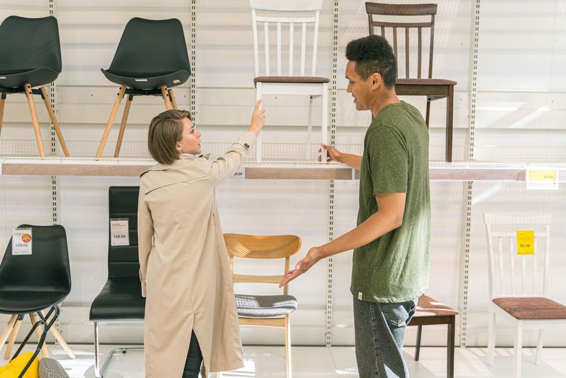 Two people comparing chairs in a furniture store, with several chairs displayed on shelves.