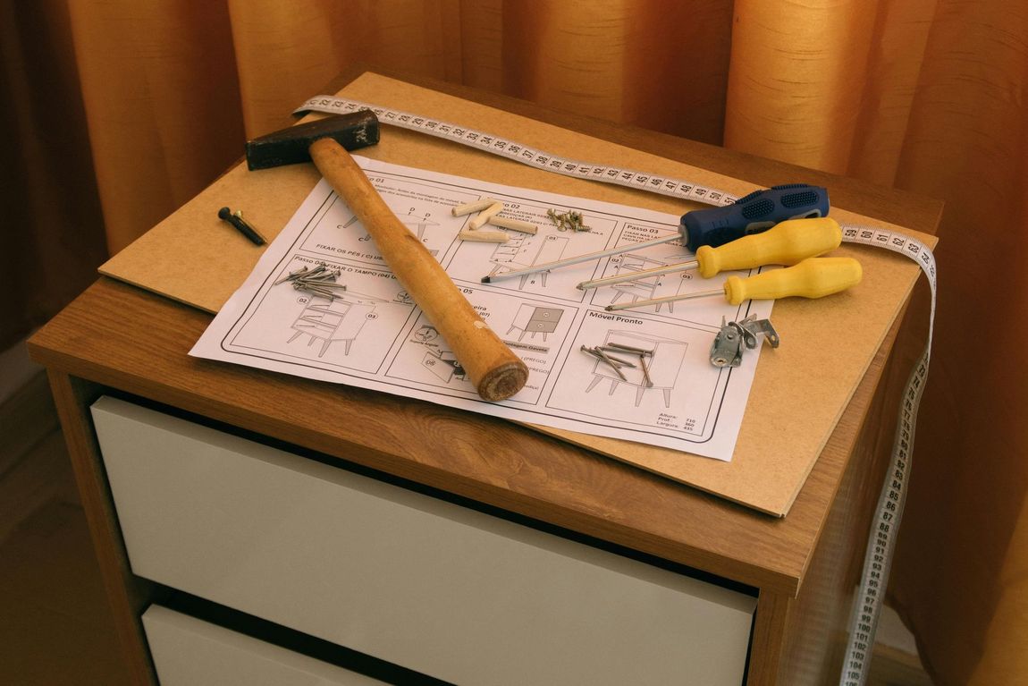 Hand tools and a rolled plan on a small wooden cabinet in a workshop setting
