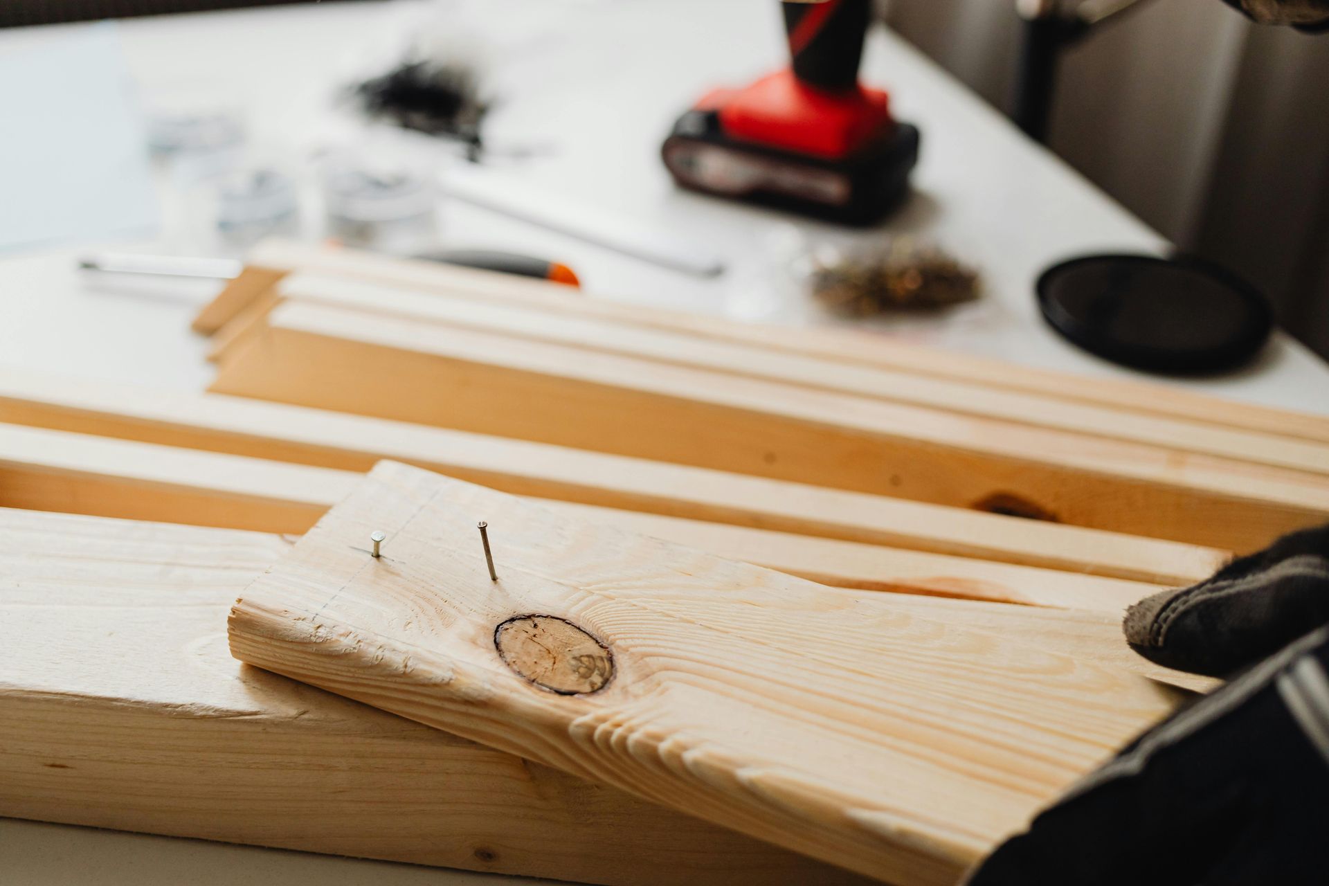 Wooden planks and a ruler on a workbench, with a red tool and black cup in the background