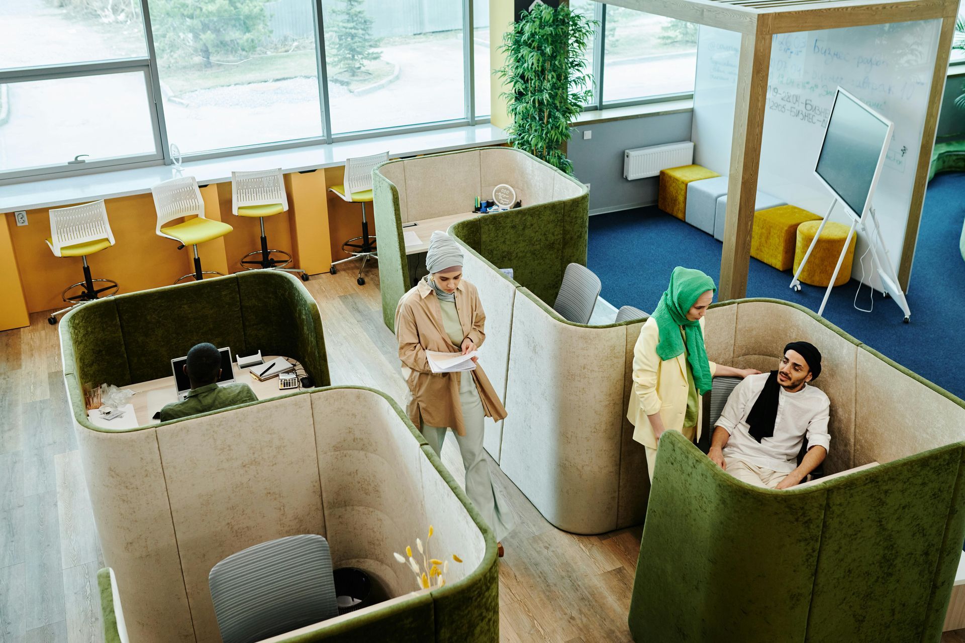 People meeting in a modern office with green partitioned cubicles and large windows.