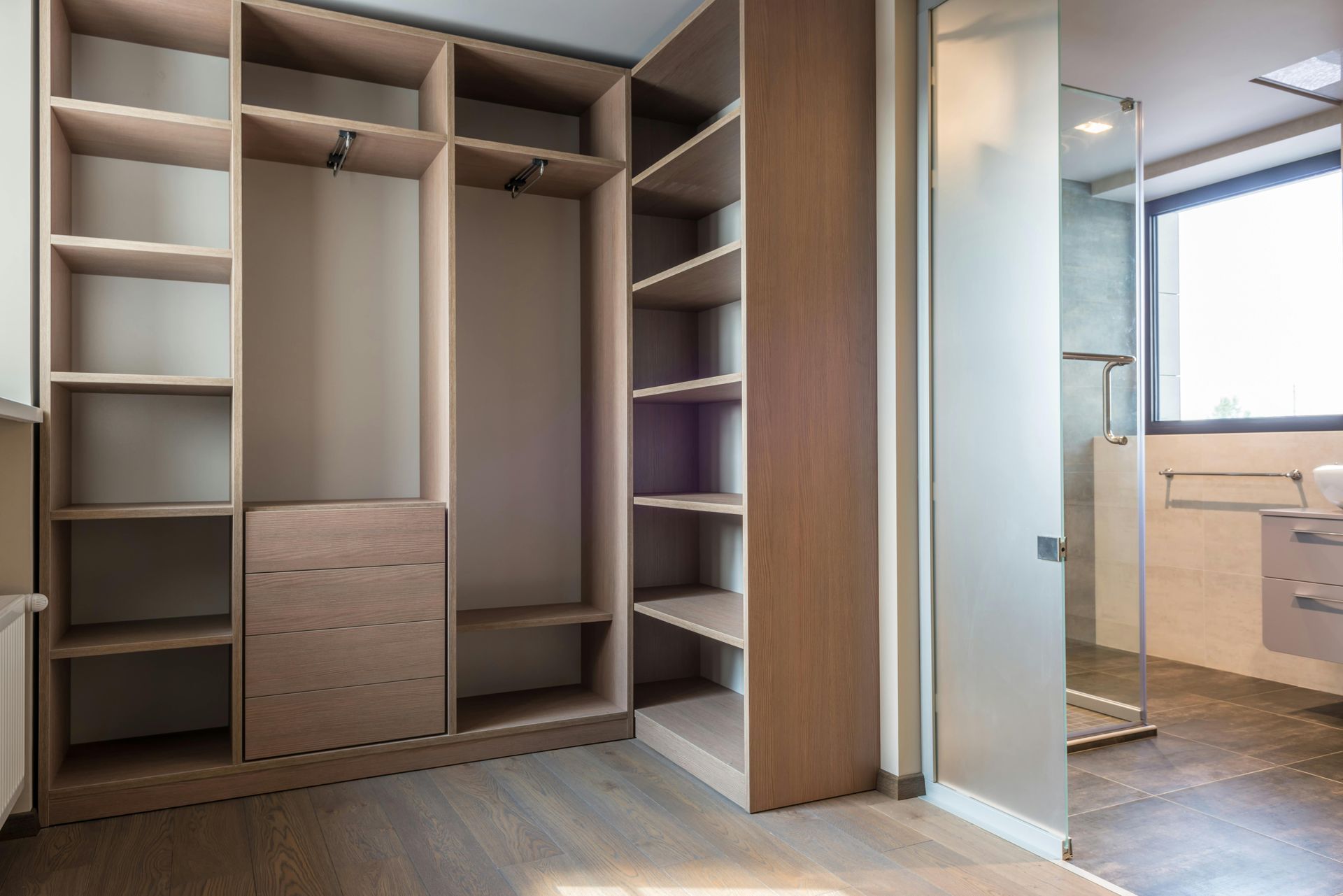 Empty walk-in closet with shelves and drawers. Light wood finish. A bathroom is partially visible.