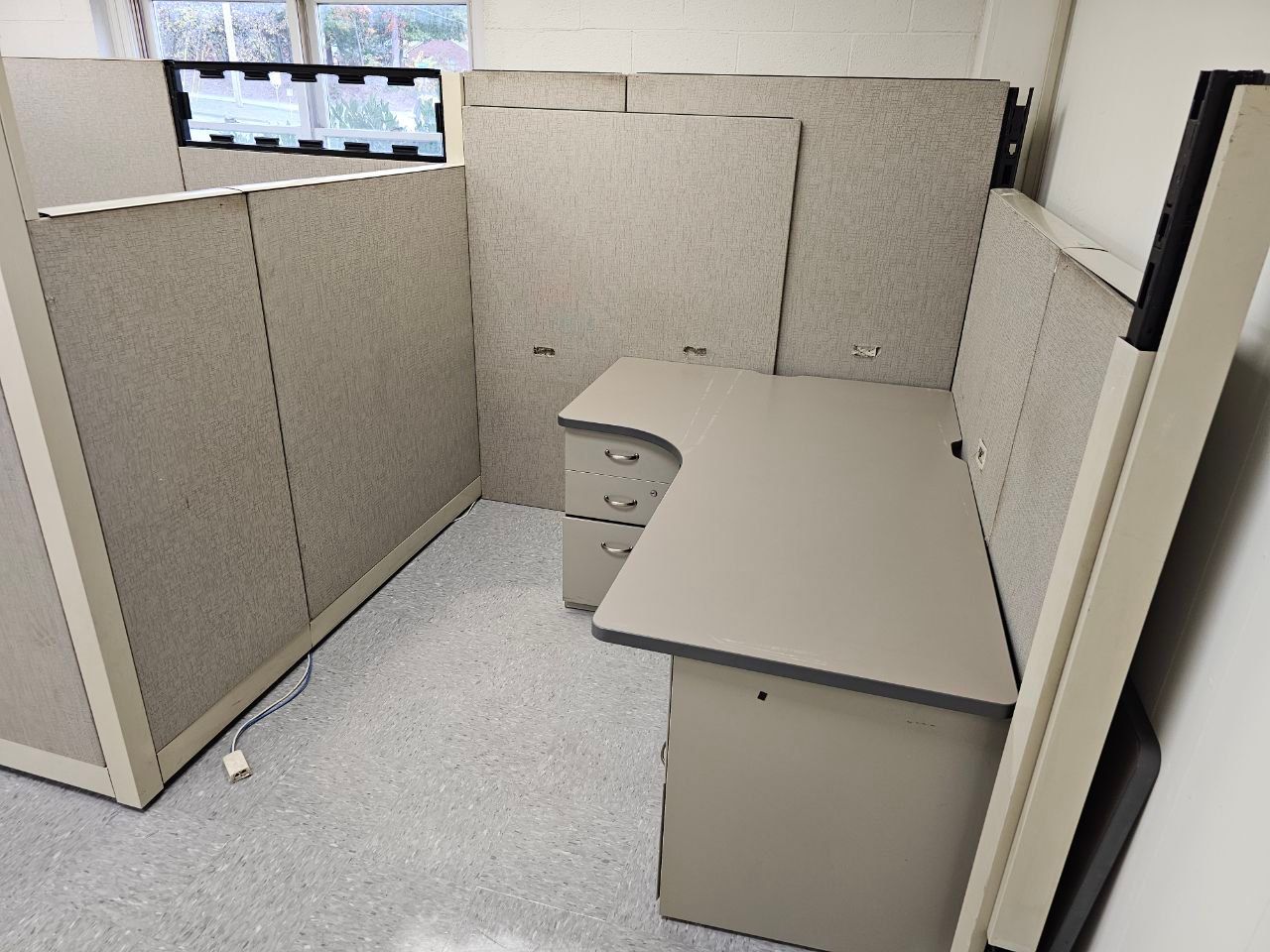 Empty beige office cubicle with L-shaped desk and gray carpet flooring