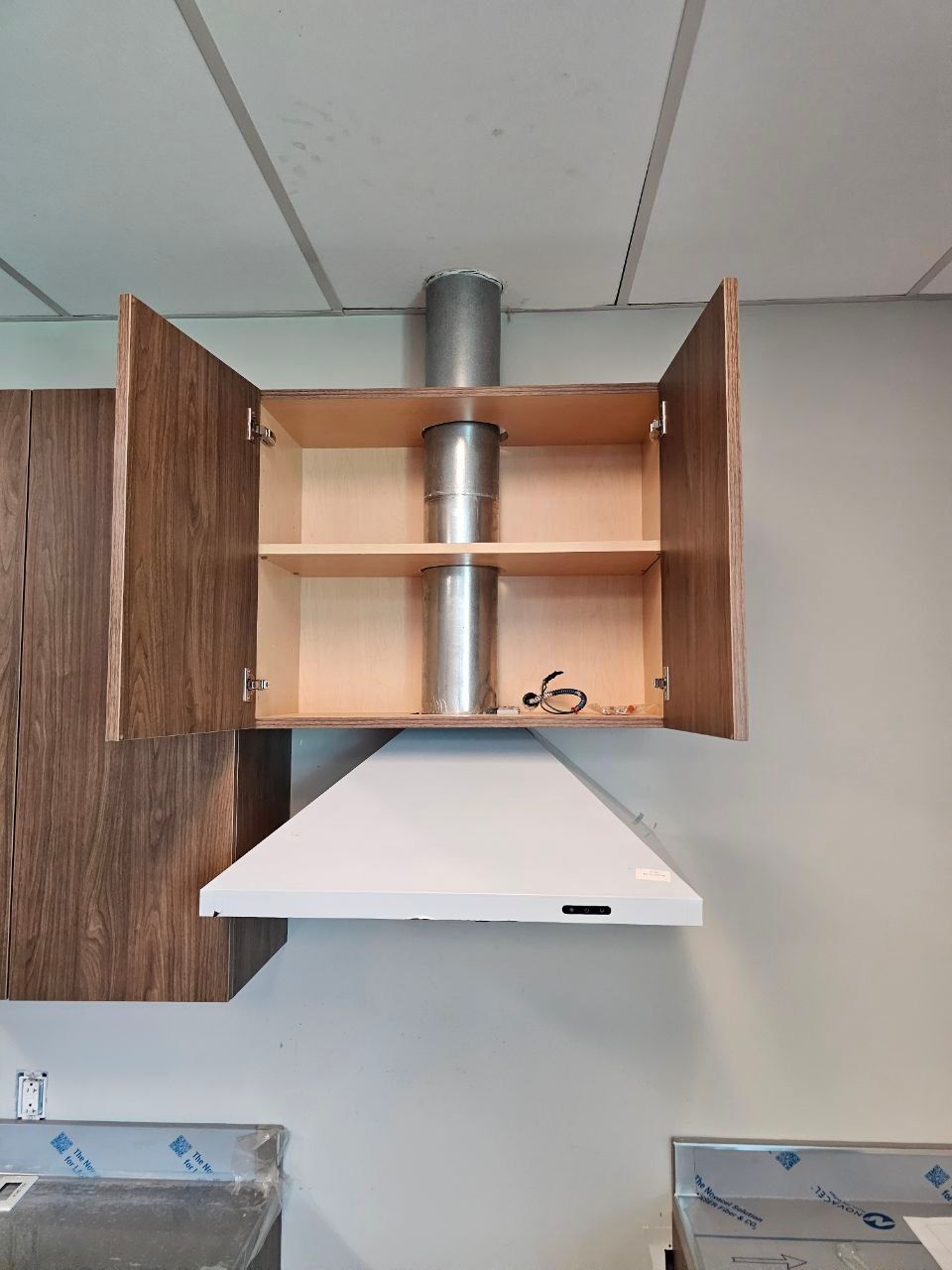 White range hood below an open cabinet with a metal exhaust pipe.