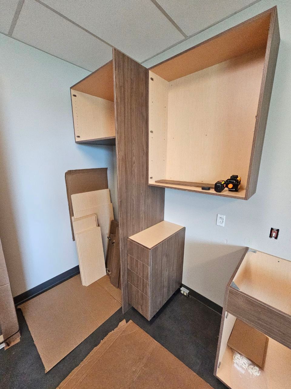 Cabinets being installed in a corner. Unfinished wood cabinets and panels are against a light blue wall.