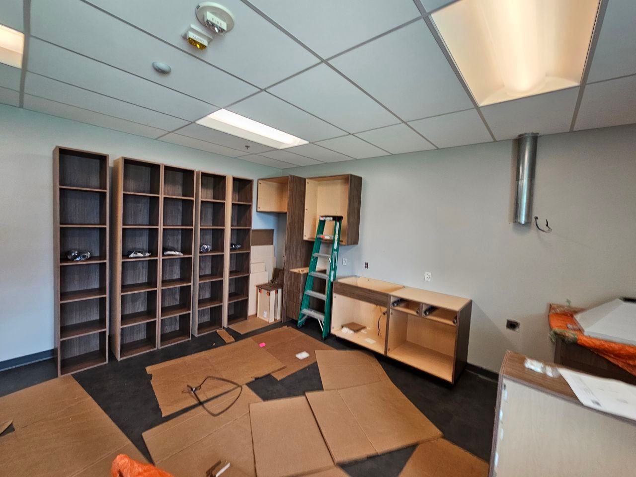 Unfinished room with shelves and cabinets, construction materials on floor, and a ladder.