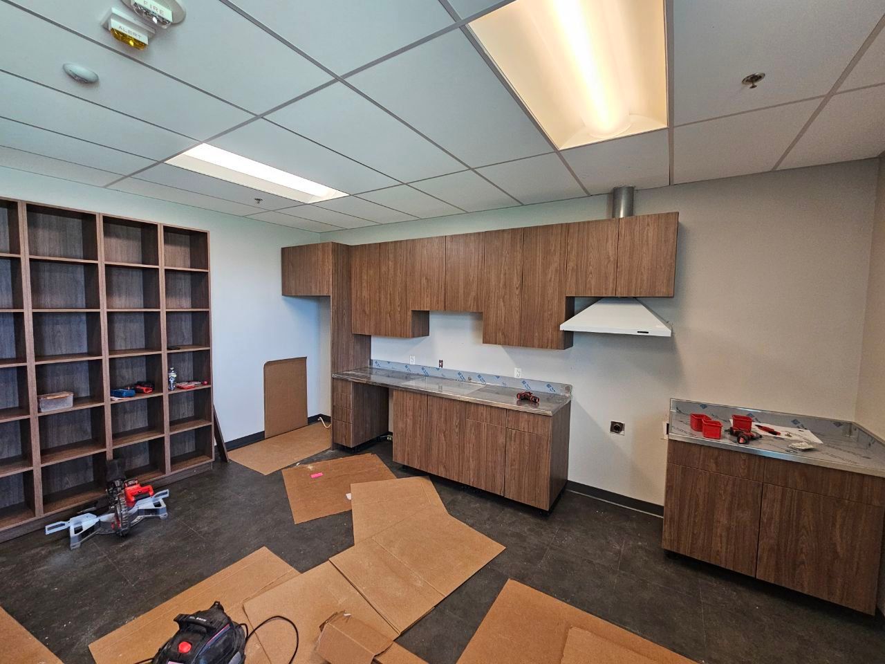 Interior view of a room with kitchen cabinets and shelving; construction in progress, cardboard on the floor.