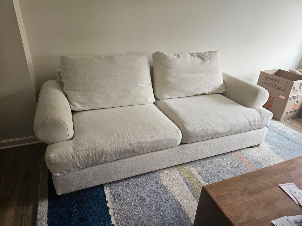White loveseat with two large seat cushions and two back pillows on a blue rug.