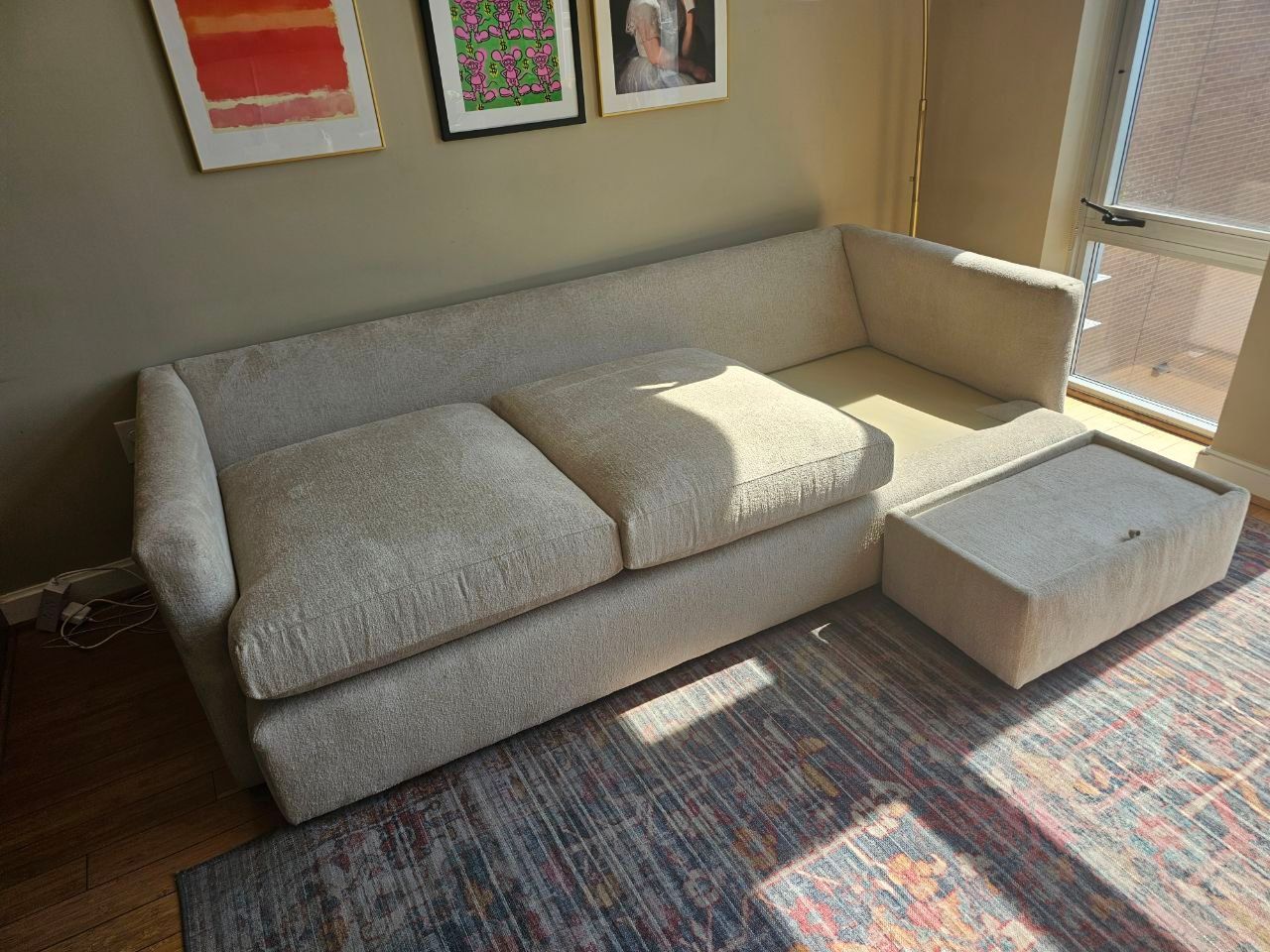 Light gray sectional sofa with matching ottoman in a sunlit living room near a window and rug
