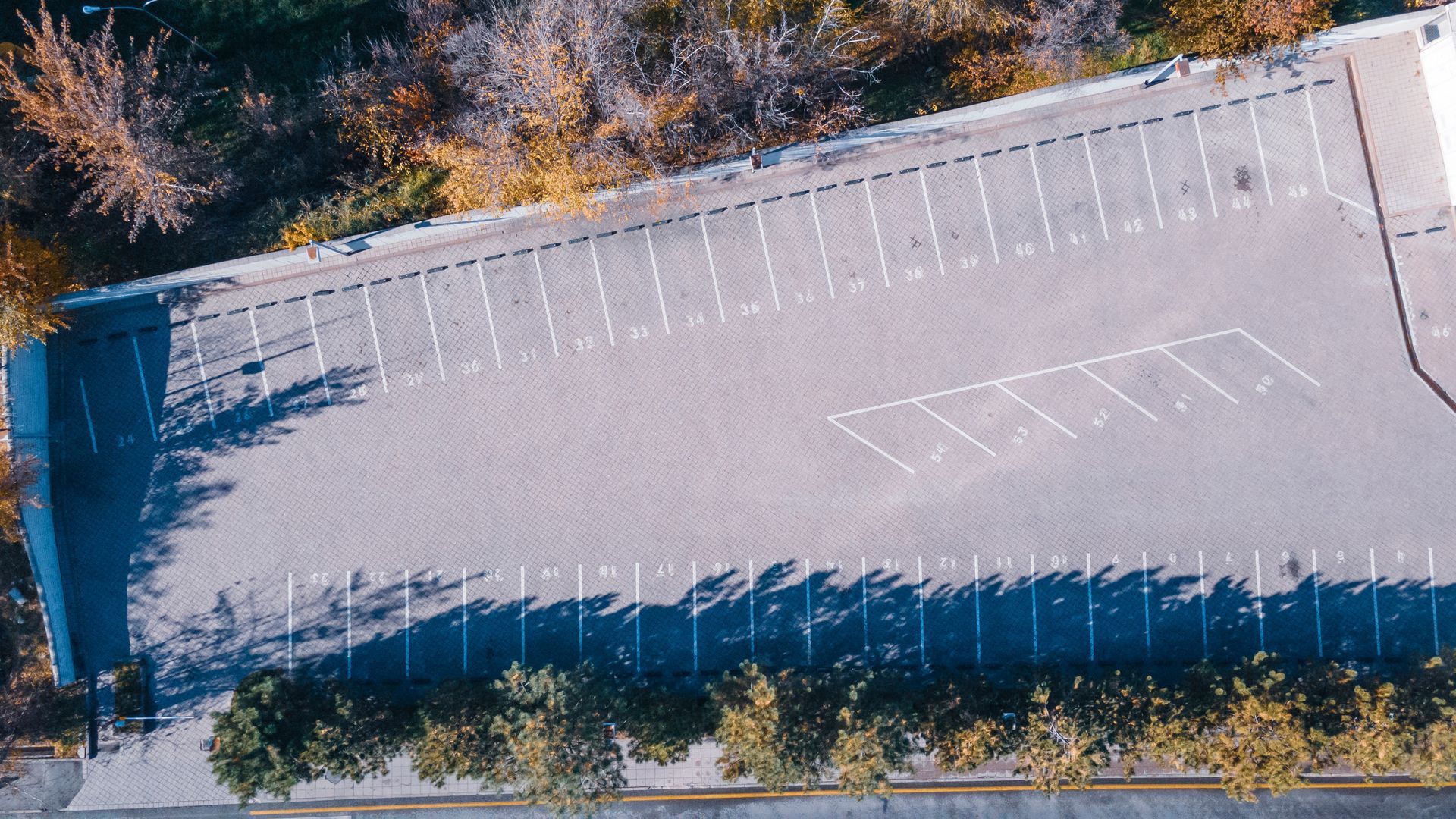 An aerial view of an empty parking lot with trees in the background.