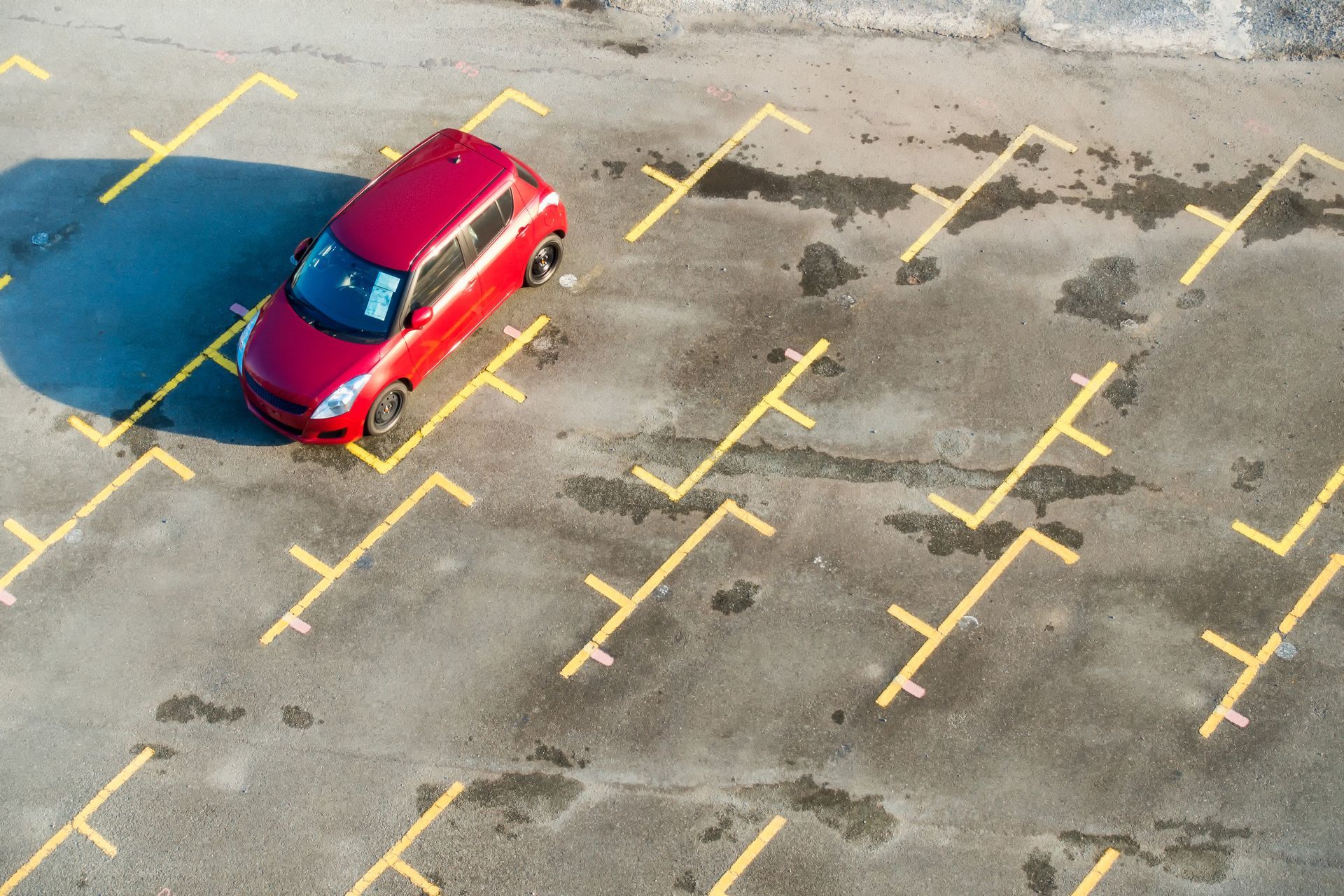 A red car is parked in a parking lot with yellow lines.